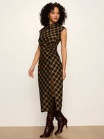 Sanctuary Autumn Edit Dress in Autumn Goldie Plaid — black and gold bias-cut midi dress with mock neck, twist waist detail, and front slit, styled with dark brown knee-high boots.