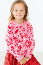 Mila Candy Canes Sweater in pink with red candy cane pattern, worn by young girl with red sequin skirt, front view.