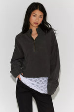 Free People Celeste Quarterzip in washed black ribbed fabric with gold half-zip, worn over white lace top with black jeans, front view on model.