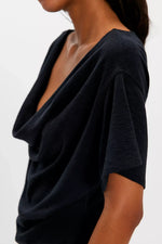 Free People Waterfall Cowl in Black — close-up side view on model showing draped cowl neckline and short sleeve detail