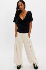 Free People Waterfall Cowl in Black — deep draped cowl neckline, short sleeves, fitted silhouette, worn by model with wide-leg cream trousers.