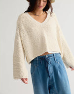 Free People Heartland Pullover in Tofu, a cropped cream V-neck knit sweater with wide sleeves, worn by a model with a crochet bucket hat