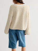 Free People Heartland Pullover in Tofu, back view on model wearing denim shorts and crochet bucket hat, cream boucle knit sweater