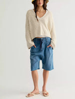 Free People Heartland Pullover in Tofu, a cream V-neck loose knit sweater worn by a model with denim shorts and a yellow bucket hat