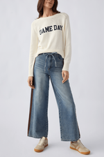 Z SUPPLY Varsity Stand In Sweater in cream/sandstone with navy 'Game Day' lettering, worn by model with wide-leg jeans and cap, front view.