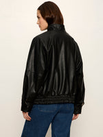 Sanctuary Alana Jacket in black faux leather, back view on model, featuring elastic hem, ribbed cuffs, and relaxed bomber silhouette with blue jeans