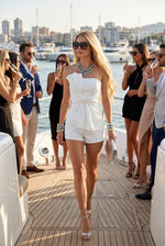 Baby Pink Strapless Stretch Cotton Denim Set With Bow in White, model wearing white tube top with twist bow and matching mini shorts on yacht deck