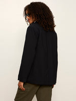 Sanctuary Maci Blazer in navy pinstripe shown from the back on a model with curly hair and sunglasses, paired with olive pants
