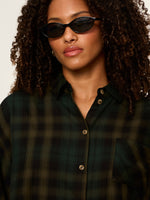Sanctuary Autumn Edit Flannel in Forest Plaid — dark green and black plaid button-front shirt with chest pocket, worn by model with curly hair and cat-eye sunglasses.