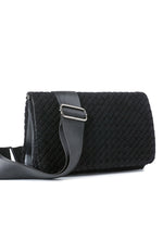Haute Shore Lexi Woven Crossbody in Jet Black — angled view showing woven texture, flap closure, and gray nylon strap with silver hardware