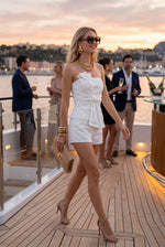 Baby Pink Strapless Stretch Cotton Denim Set With Bow in White, worn by model on yacht deck at sunset with gold accessories.