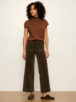 Sanctuary Chelsea Wide Leg corduroy pants in Kalamata olive green, front view on model styled with brown mock-neck top and mule slides.