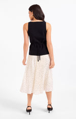 Sadie Margaux Sweater Waistcoat in black, back view on model, featuring tie waist detail, paired with cream polka dot pleated skirt