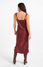 Sadie Ceremony Midi Skirt in dark wine satin, back view on model styled with matching cami top and brown knee-high boots.