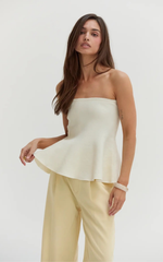 Crescent Bella Jacquard Knit Peplum Top in Cream, strapless style with flared hem, worn by model with pale yellow wide-leg trousers, front view.