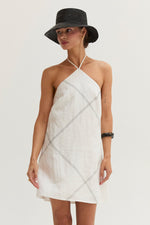Crescent Lena Linen Contrast Stitch Halter Mini Dress in White, front view on model with black straw hat and bracelet