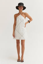 Crescent Lena Linen Contrast Stitch Halter Mini Dress in White, front view on model with black hat and flip flops