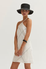 Crescent Lena Linen Contrast Stitch Halter Mini Dress in white, front view on model with black straw hat and gold accessories