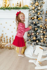 Mila Candy Canes Sweater in pink with red candy cane print, worn by a girl with a red skirt decorating a Christmas tree