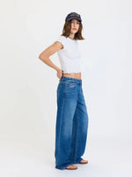 Daze Denim 2K Mid Rise Relaxed Baggy jeans in medium blue wash, worn by model with white crop top and navy cap, side view