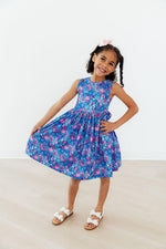 Young girl wearing Mila & Rose Tank Twirl Dress in blue floral Dreaming Daisies print, posing with hands on hips