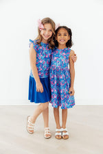 Two girls wearing Mila & Rose Tank Twirl Dresses in blue Dreaming Daisies floral print, standing together smiling