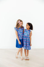 Two girls wearing Mila & Rose Tank Twirl Dresses in Dreaming Daisies blue floral print, standing together smiling