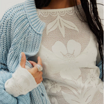 Free People Delilah Long Sleeve in Clean Ivory — white floral pointelle knit top worn by model layered under a light blue chunky cardigan.