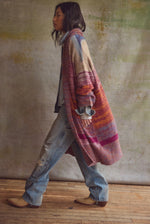 Free People Enid Cardi in Ocean Sunset Combo, colorful striped oversized knit cardigan worn by model with wide-leg jeans, side view.
