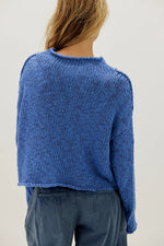 Free People Opal Sweater in Peri Blue — back view, chunky knit, cropped length, raw hem, worn with blue trousers.