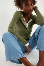 Free People Jamie Henley in Capulet Olive, ribbed long-sleeve top with snap buttons, layered over white shirt, paired with wide-leg jeans.