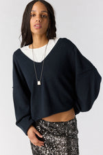 Free People See Me V-Neck Pullover in black, cropped oversized sweater with balloon sleeves, worn over white tee with sequin skirt, front view on model.