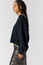 Free People See Me V-Neck Pullover in black, side view on model styled with silver sequin skirt, cropped silhouette with ribbed cuffs