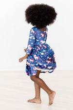 Mila Painted Skies Twirl Dress in blue unicorn print, back view, young girl spinning barefoot showing dress flare
