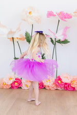 Mila & Rose Tank Tutu Dress in Purple Perfection - back view of blonde child twirling in purple tulle skirt with floral backdrop