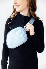 Mila Light Blue Fleece Belt Bag worn as crossbody by smiling model in black zip-up jacket, showing fluffy sherpa texture