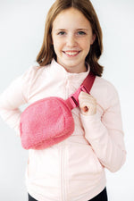 Mila Pink Fleece Belt Bag worn crossbody by a smiling young girl in a light pink zip-up jacket, front view.