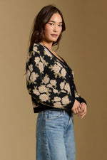 Saltwater Luxe Calian Sweater in black floral knit cardigan with tan rose pattern, worn by model with light wash jeans, side view.