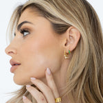 Sahira Viola Emerald CZ Huggies — gold hoop earrings with green emerald baguettes and dangling crystal charms, worn by model