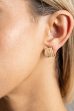 Sahira Avery CZ Huggies in gold — multi-band huggie earring with pavé crystals worn on model's ear, close-up side view.