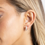 Sahira Dakota Mini Hoops in silver with baguette crystals worn on a model's earlobe, close-up side view.
