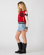 Steve Madden Rooney Jacket in red and cream varsity style with 'S' and 'NY' patches, worn by model with denim mini skirt and black boots