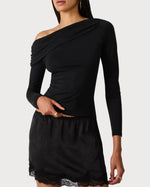 Steve Madden Ryder Knit Top in black, asymmetric one-shoulder long-sleeve style with drape detail, worn by model with lace mini skirt
