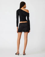 Steve Madden Ryder Knit Top in black, back view on model, one-shoulder asymmetric drape with long sleeve, paired with lace mini skirt.