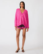Steve Madden Finley Sweater in hot pink, oversized V-neck cardigan with gold buttons and front pockets, worn by model with mini shorts