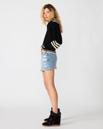 Steve Madden Dara Sweater in black with cream stripe trim, worn by model with denim mini skirt and black wedge sneakers, side view.