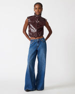 Steve Madden SC01142 cropped patent leather vest in Deep Fig dark burgundy, worn by model with wide-leg blue jeans, front view.