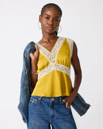 Steve Madden SC09035 satin cami top in Oilslick mustard yellow with cream lace trim, worn by model with blue jeans and denim jacket.