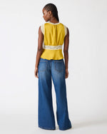 Steve Madden SC09035 top in Oilslick — back view on model, mustard yellow satin with cream lace trim, paired with wide-leg jeans.