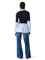 Steve Madden Lenny Knit Top back view on model — navy ribbed knit bodice with light blue poplin peplum hem and sleeves, paired with wide-leg jeans.